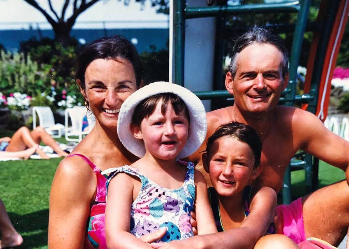 A family portrait with two adults and two children, smiling outdoors.