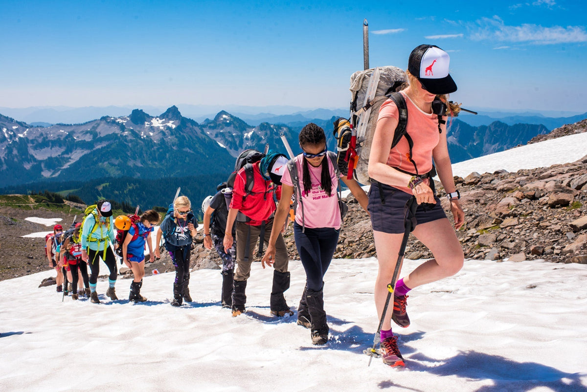 A group of women hiking on a snowy mountain trail with backpacks and gear.