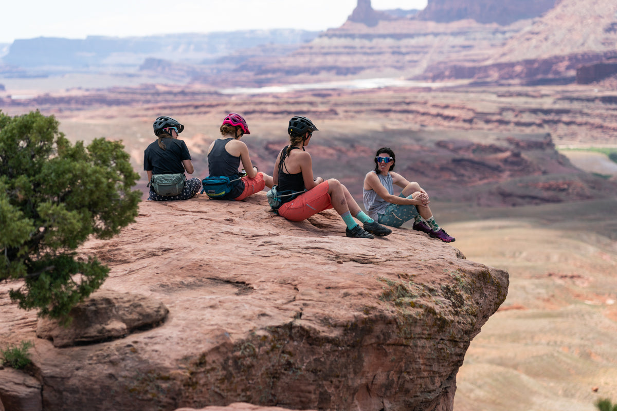 Four women sitting on a rock ledge overlooking a canyon landscape