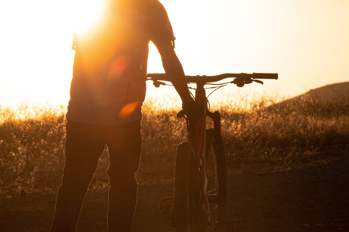Silhouette of a person holding a mountain bike against a sunset backdrop