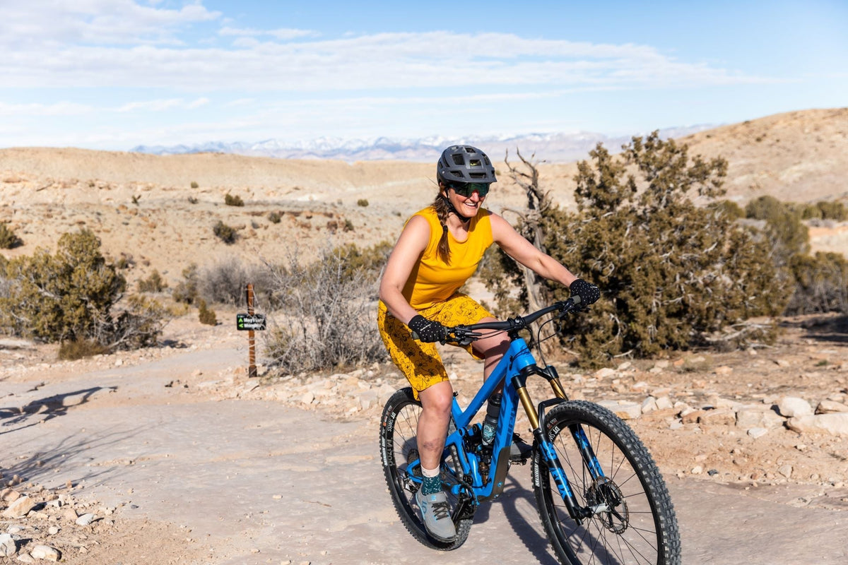 Cassie Abel riding a mountain bike on a trail with a desert landscape