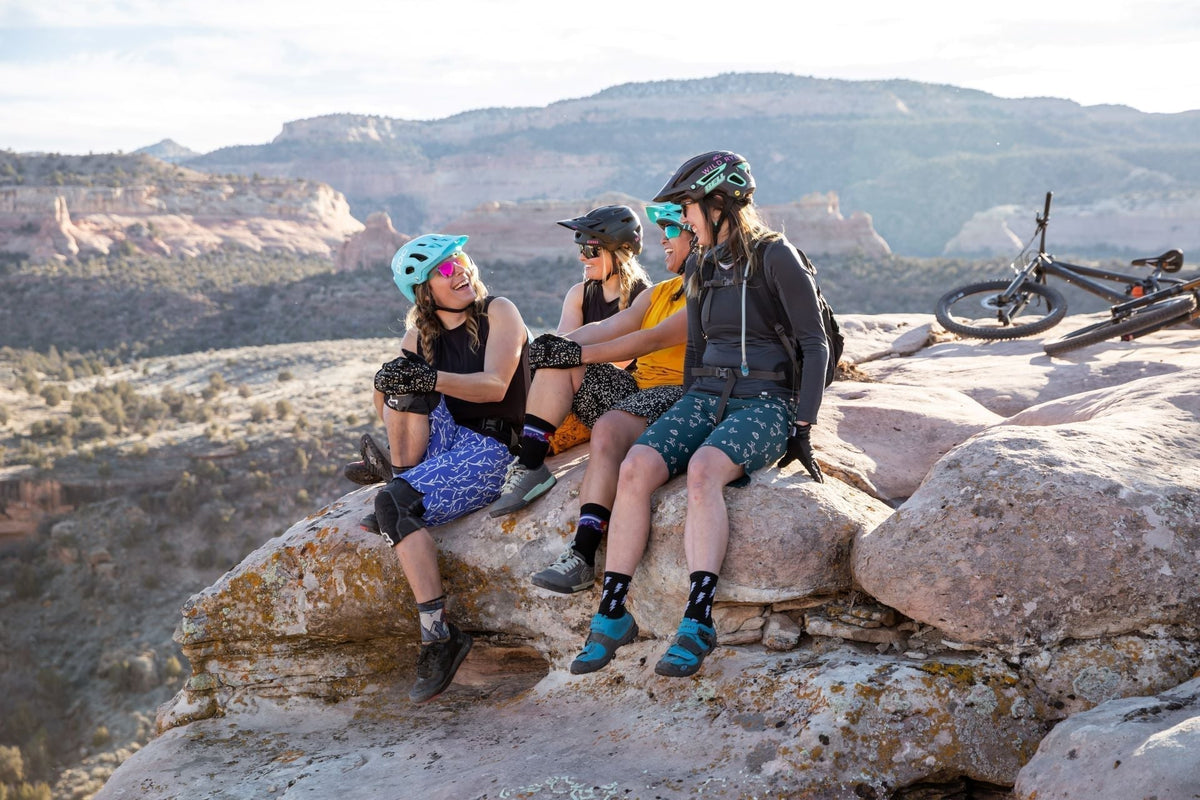 Three women in cycling gear sitting on a rock ledge, enjoying the view.