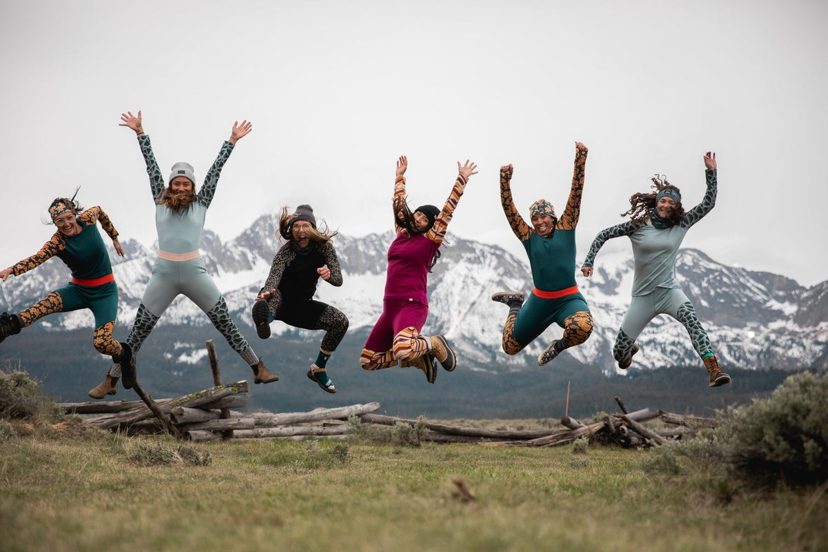 A group of women in colorful outfits jumping joyfully in a mountainous landscape.