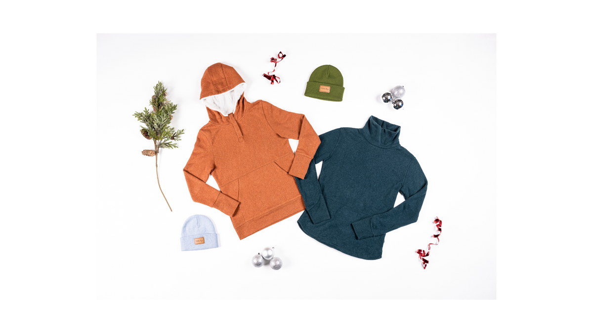 Two sweaters, one orange and one teal, with hats and decorations for a gift guide.