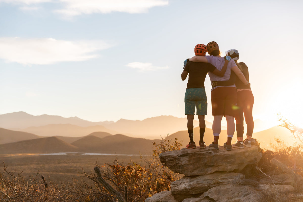 Three mountain bikers enjoying a sunset view from a rocky outcrop