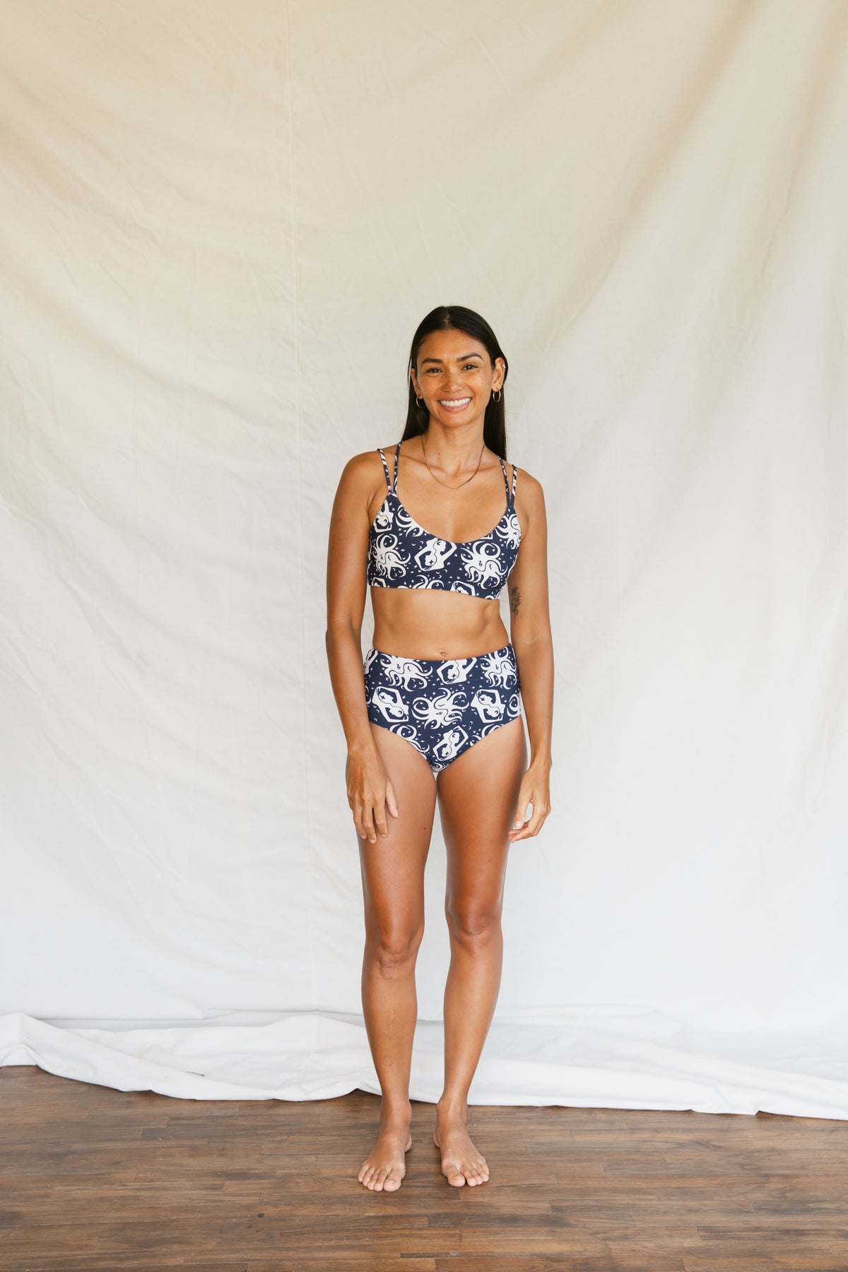Person wearing a navy blue bikini with white octopus-like pattern on a plain background, front full body view