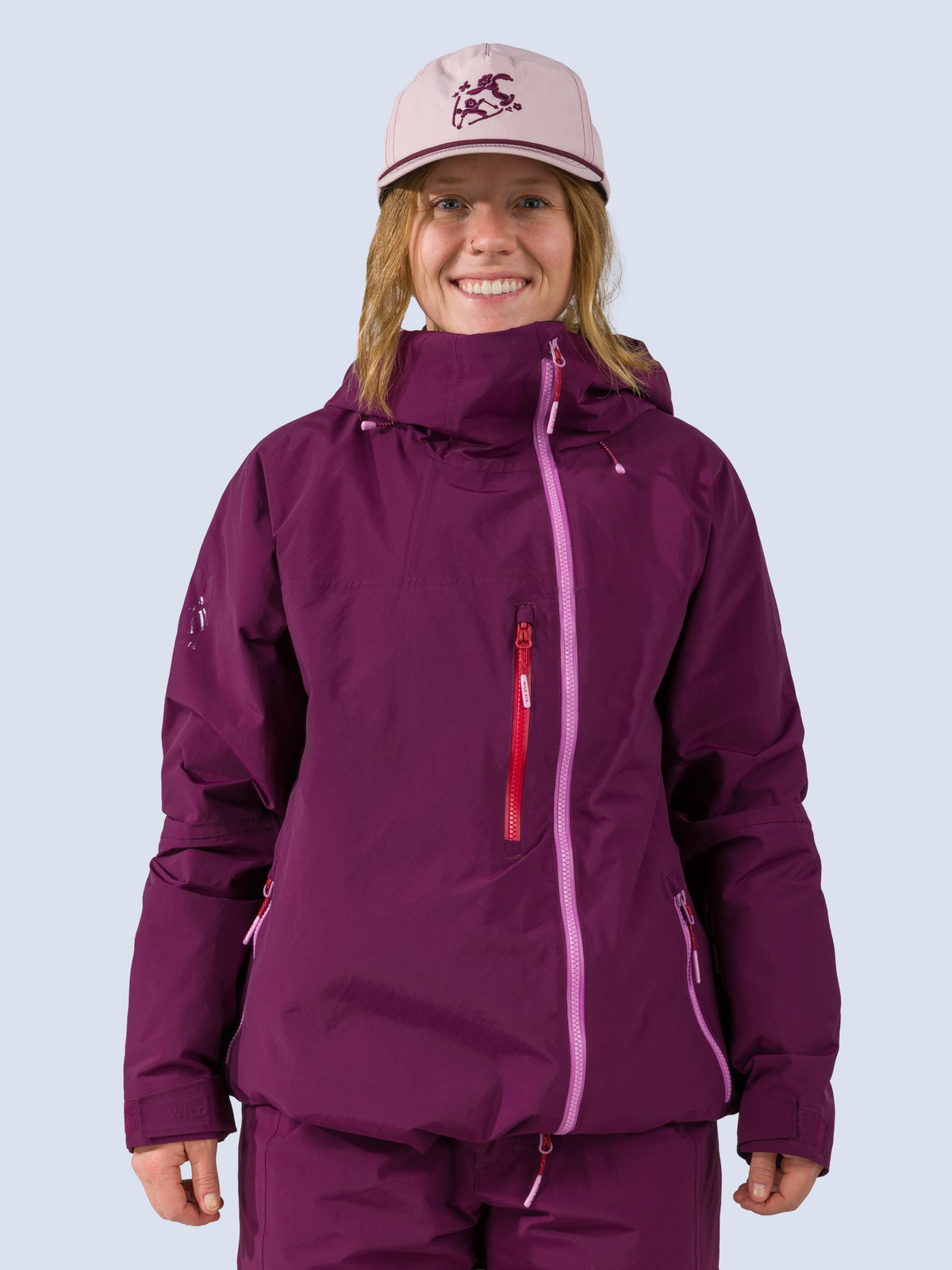 Woman wearing triumph trucker hat in schuss, a pink hat with skiers on it