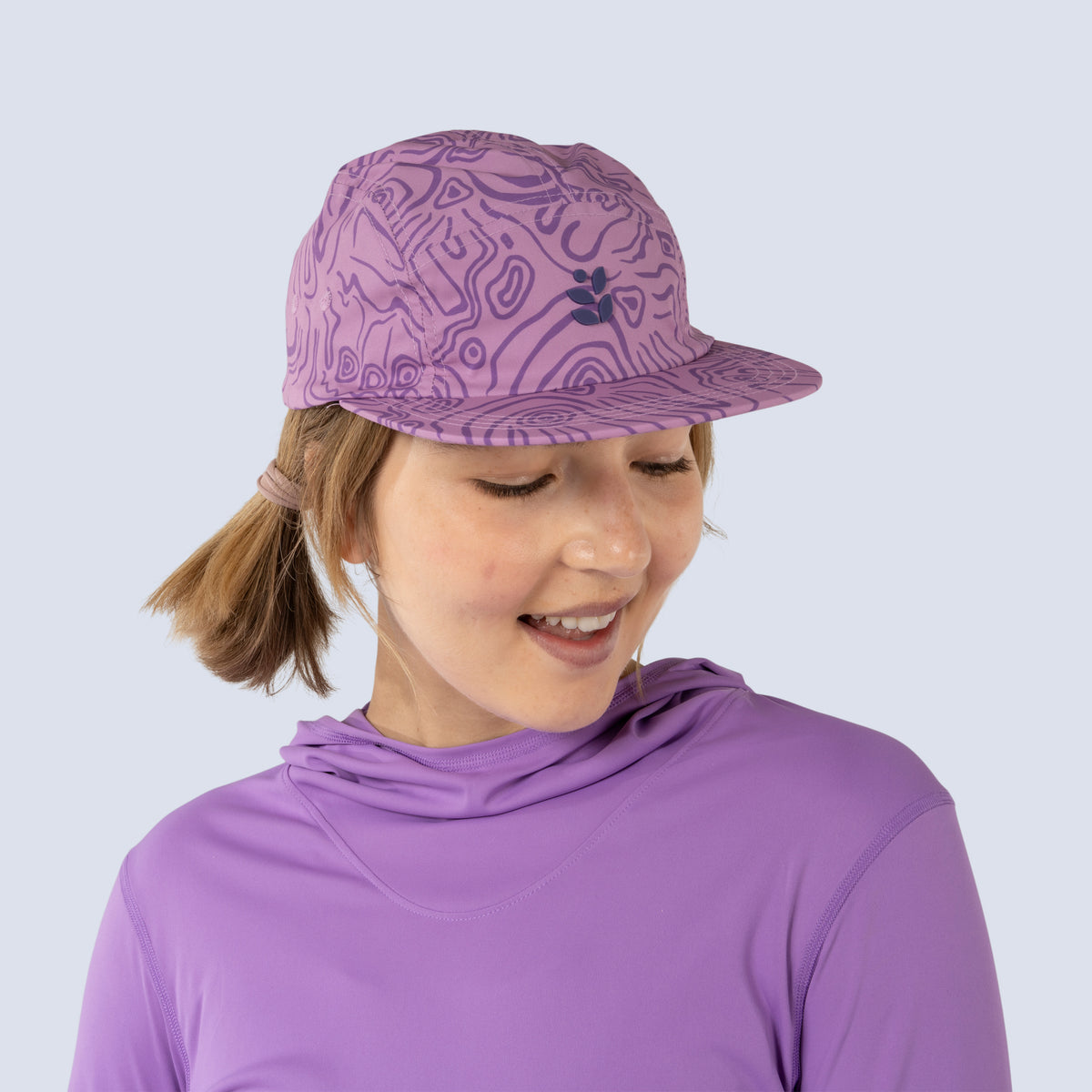 Person wearing a pink baseball cap and purple shirt, looking down and smiling
