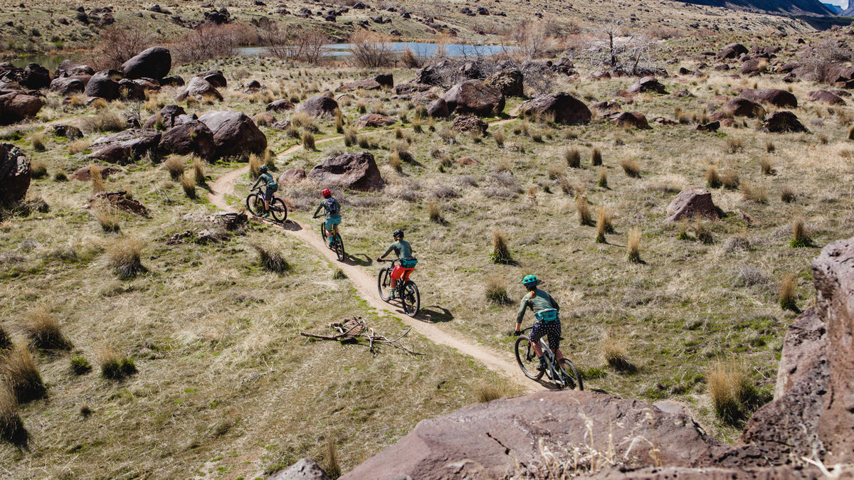 Five mountain bikers riding on a dirt trail through a rocky landscape