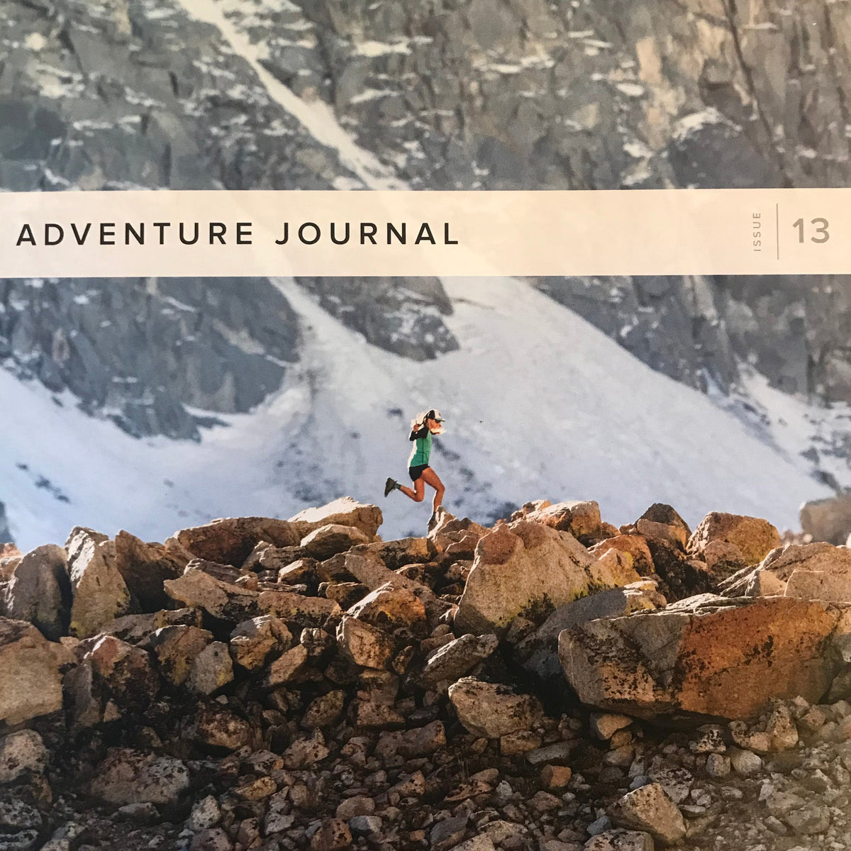A woman running on rocky terrain with mountains in the background, Adventure Journal Issue 13
