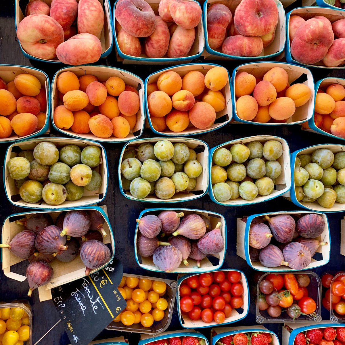 A variety of fresh fruits including peaches, apricots, figs, and tomatoes in baskets at a market.