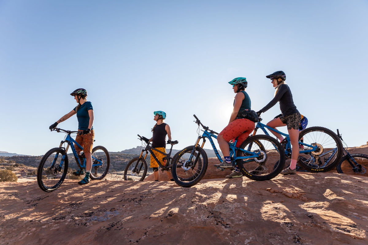 Four mountain bikers in colorful shorts on a rocky terrain under a clear sky