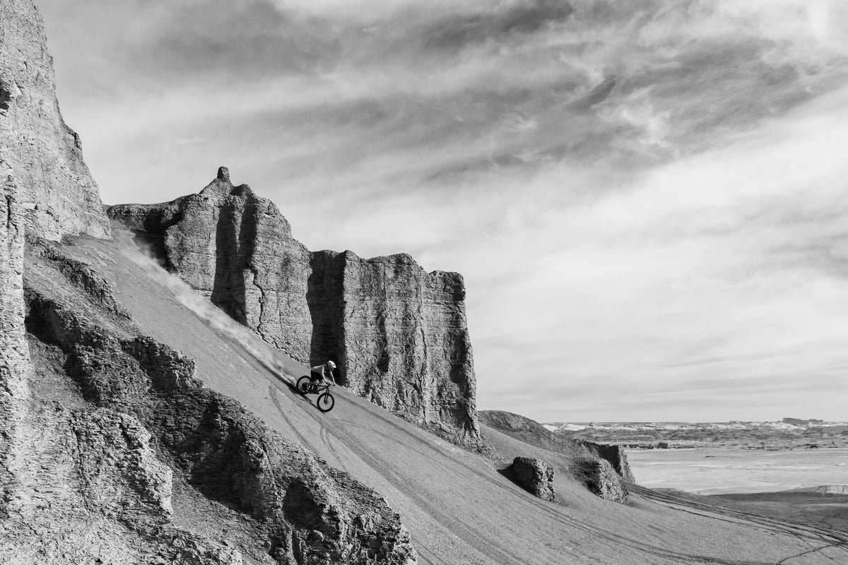A cyclist riding down a steep rocky slope against a cloudy sky