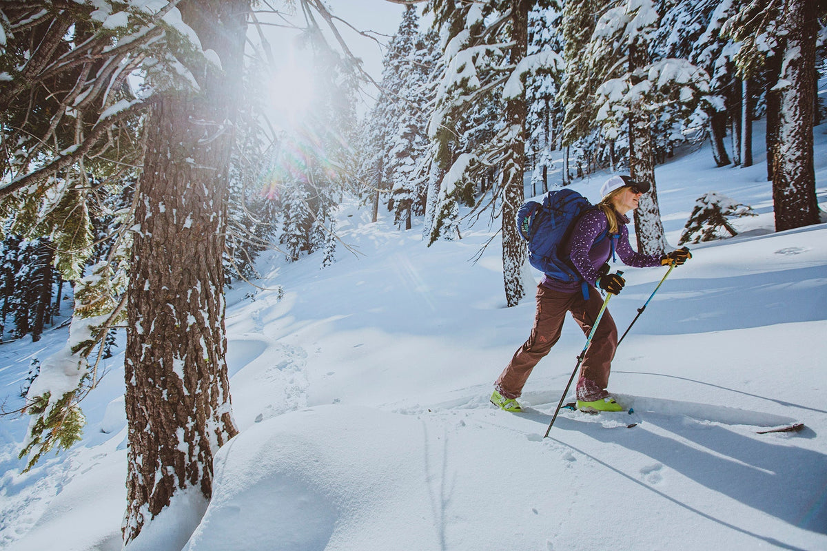 A skier ascending a snowy trail in a forested backcountry area