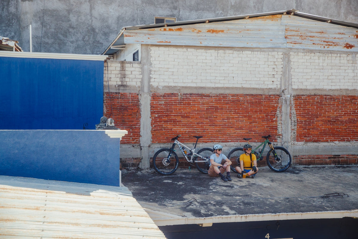 Two mountain bikers sitting on a rooftop with bikes beside them, in Oaxaca.
