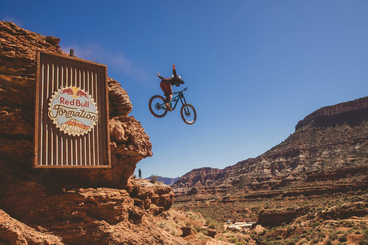 A mountain biker jumping off a rock formation at Red Bull Formation in Virgin, Utah, with a sign in the foreground.