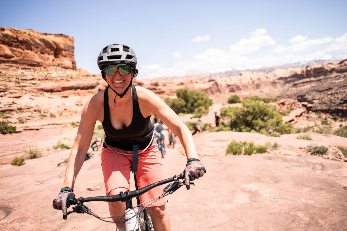 A woman mountain biking on a rocky trail with a scenic background.