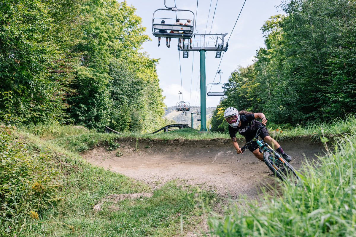 A mountain biker navigating a curve on a trail with a ski lift in the background.