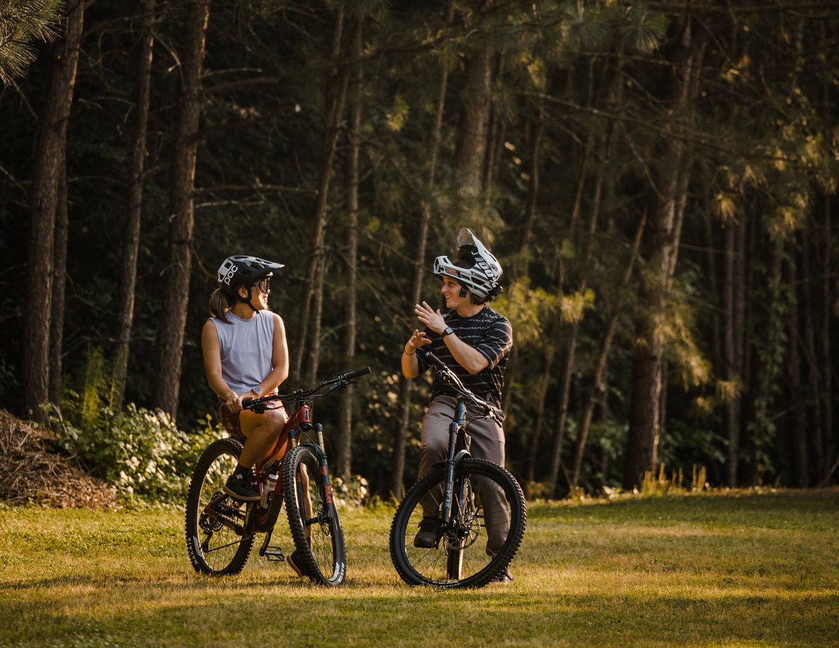 Rachel Kim and a friend chatting on mountain bikes in a forested area