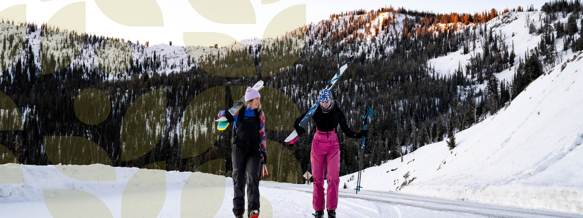 Two women skiing in a snowy landscape with mountains in the background, showcasing outdoor adventure and community spirit.