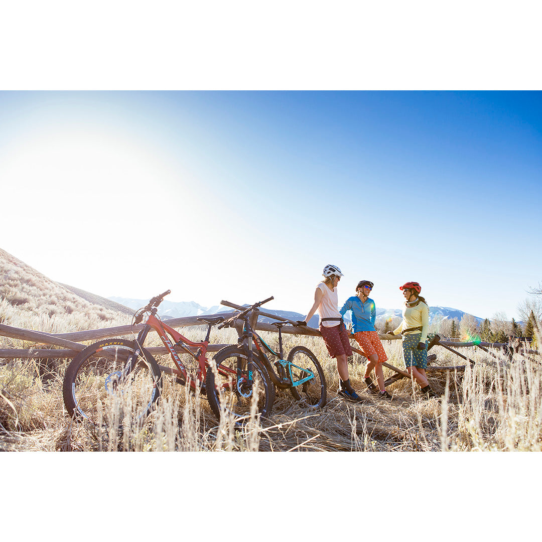 Three women in outdoor apparel standing by bicycles in a scenic landscape