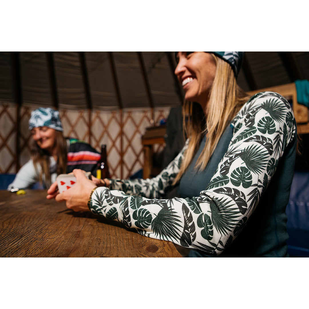 Two women in a yurt playing cards, wearing patterned long-sleeve tops.