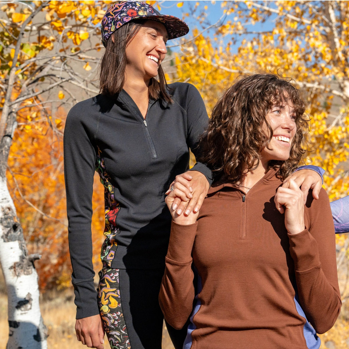 [Understory Blocked] Two women standing together in a forest with autumn foliage