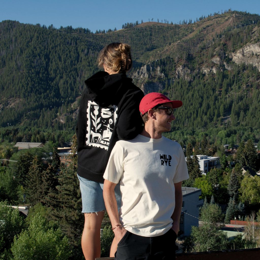 Two people standing on a hill with a scenic view of mountains and trees in the background.