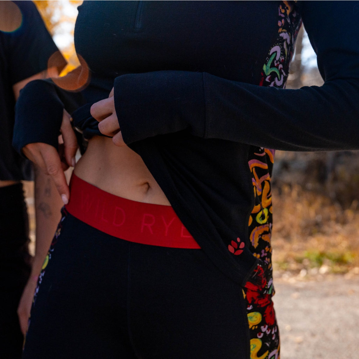 [Understory Blocked] Person wearing a black long-sleeve shirt with colorful patterns and black pants with a red waistband.