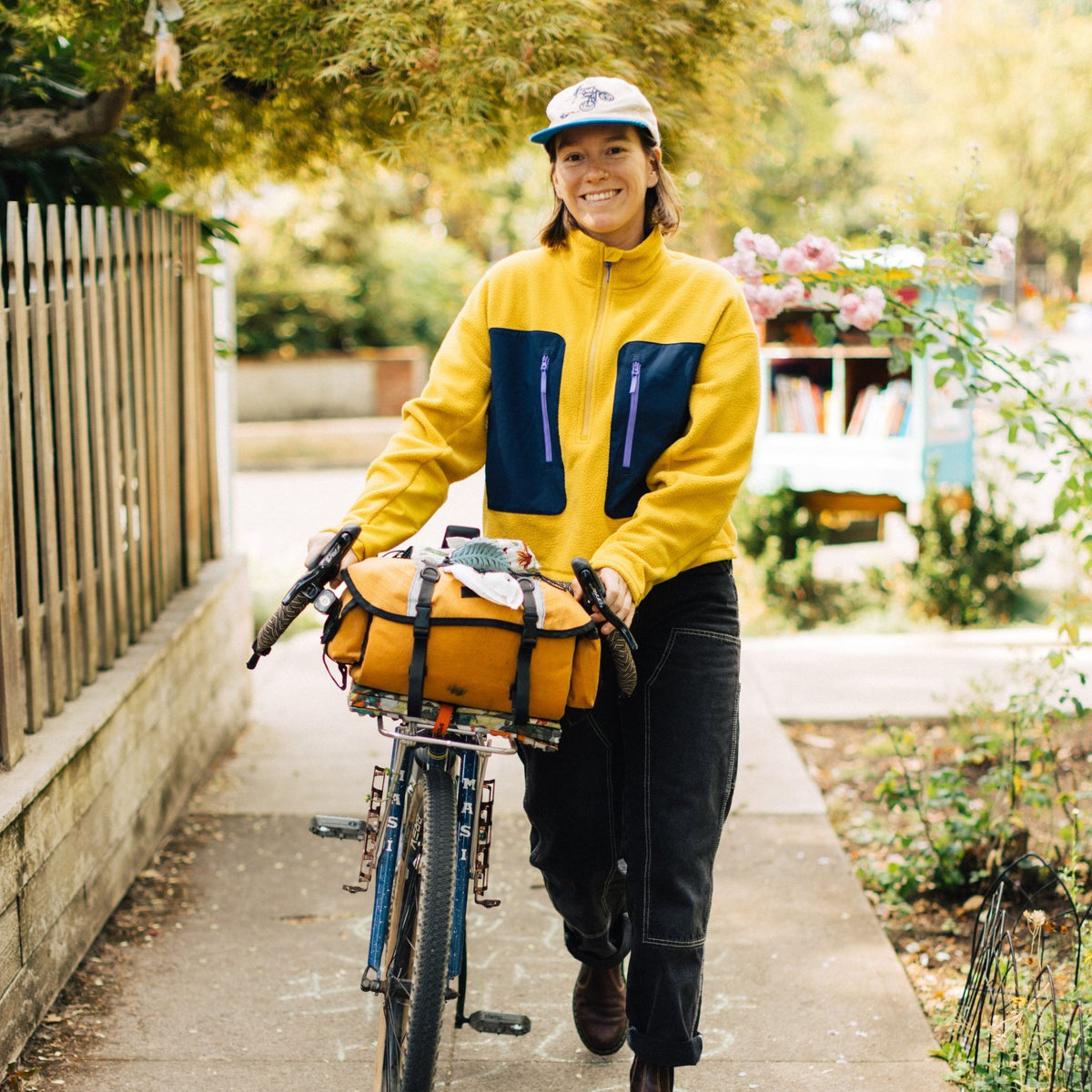[Saffron] Woman smiling and walking her bike wearing yellow fleece