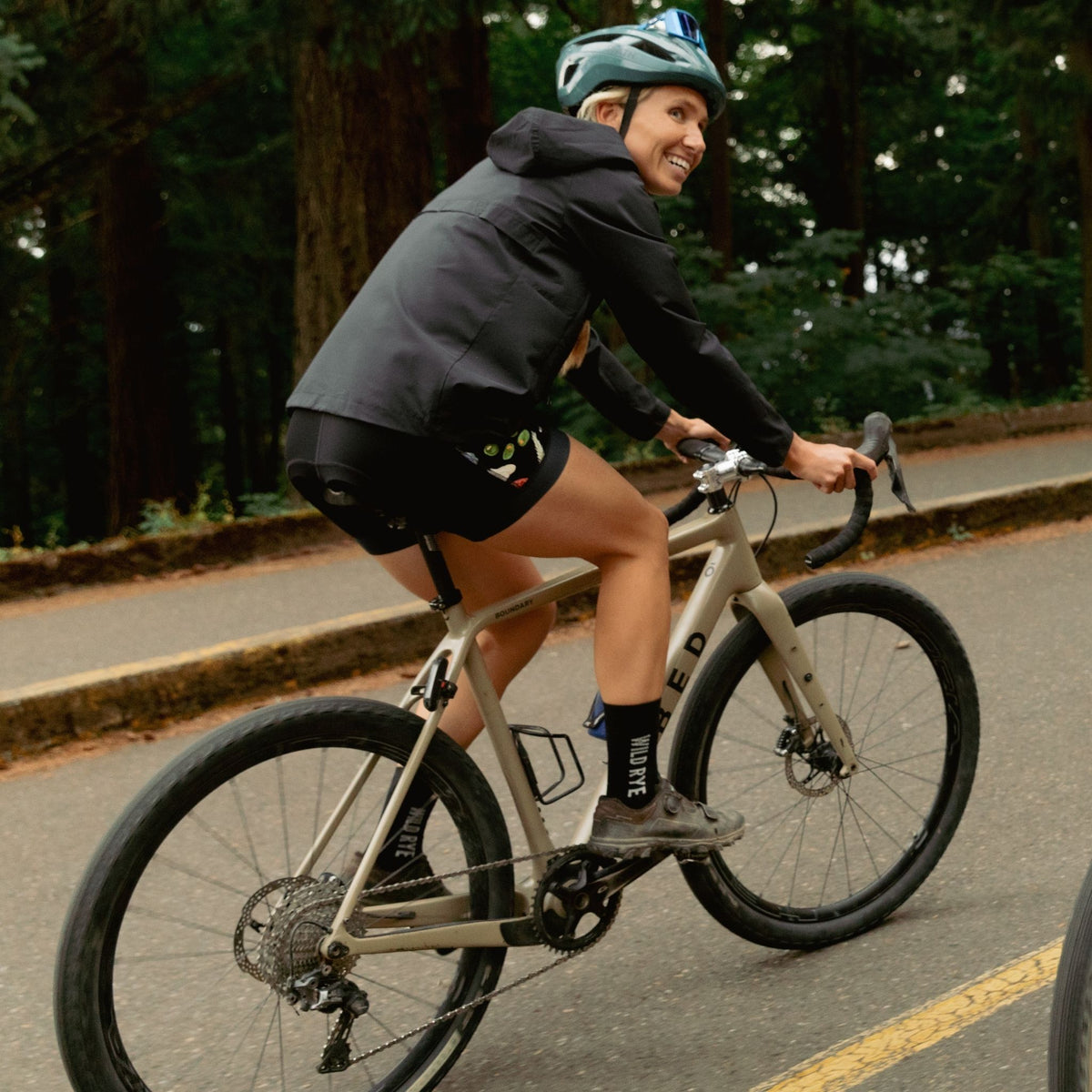 [Black] Person cycling on a road with trees in the background