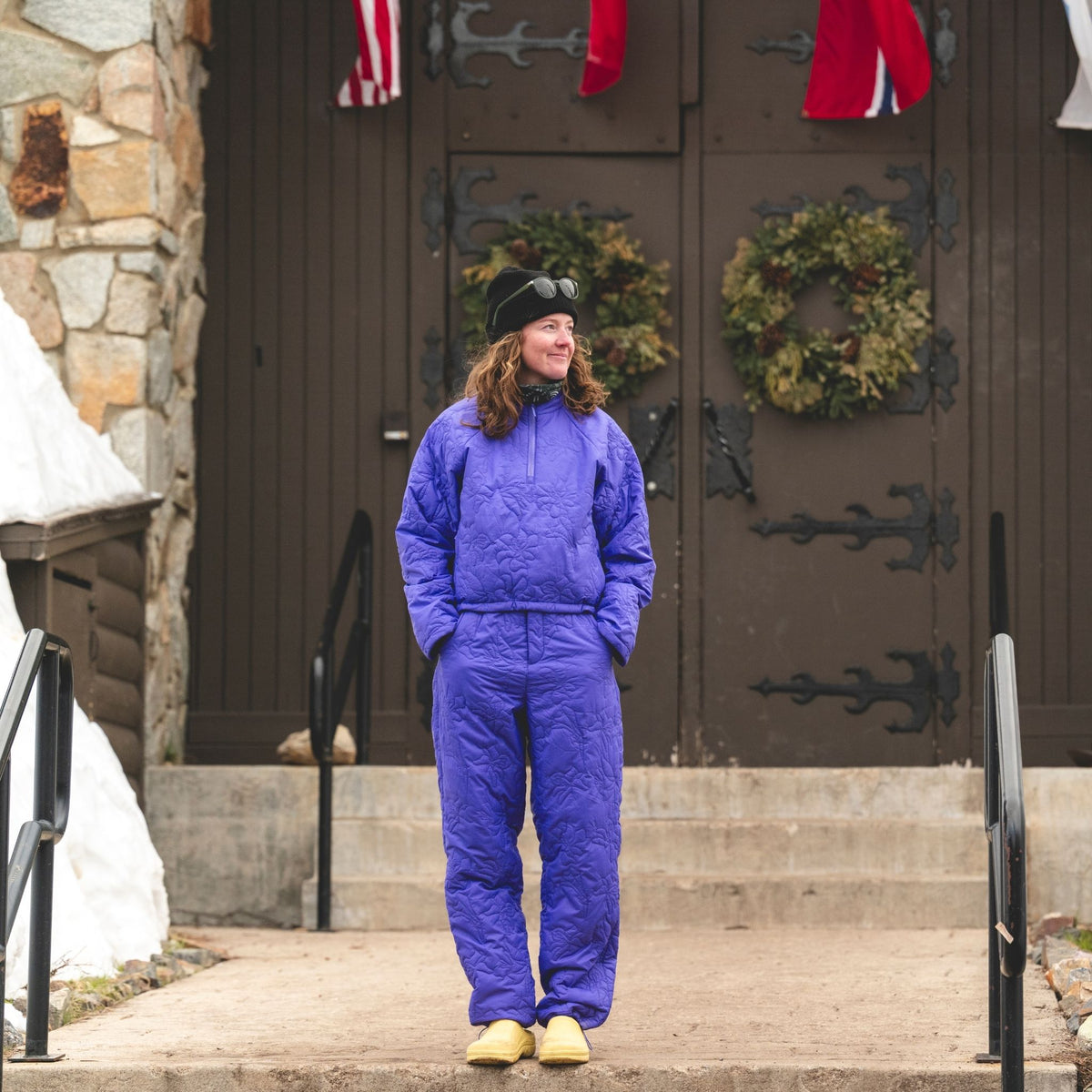 [Iris] Person wearing a a matching purple payette pullover and pant, standing in front of a door with wreaths 