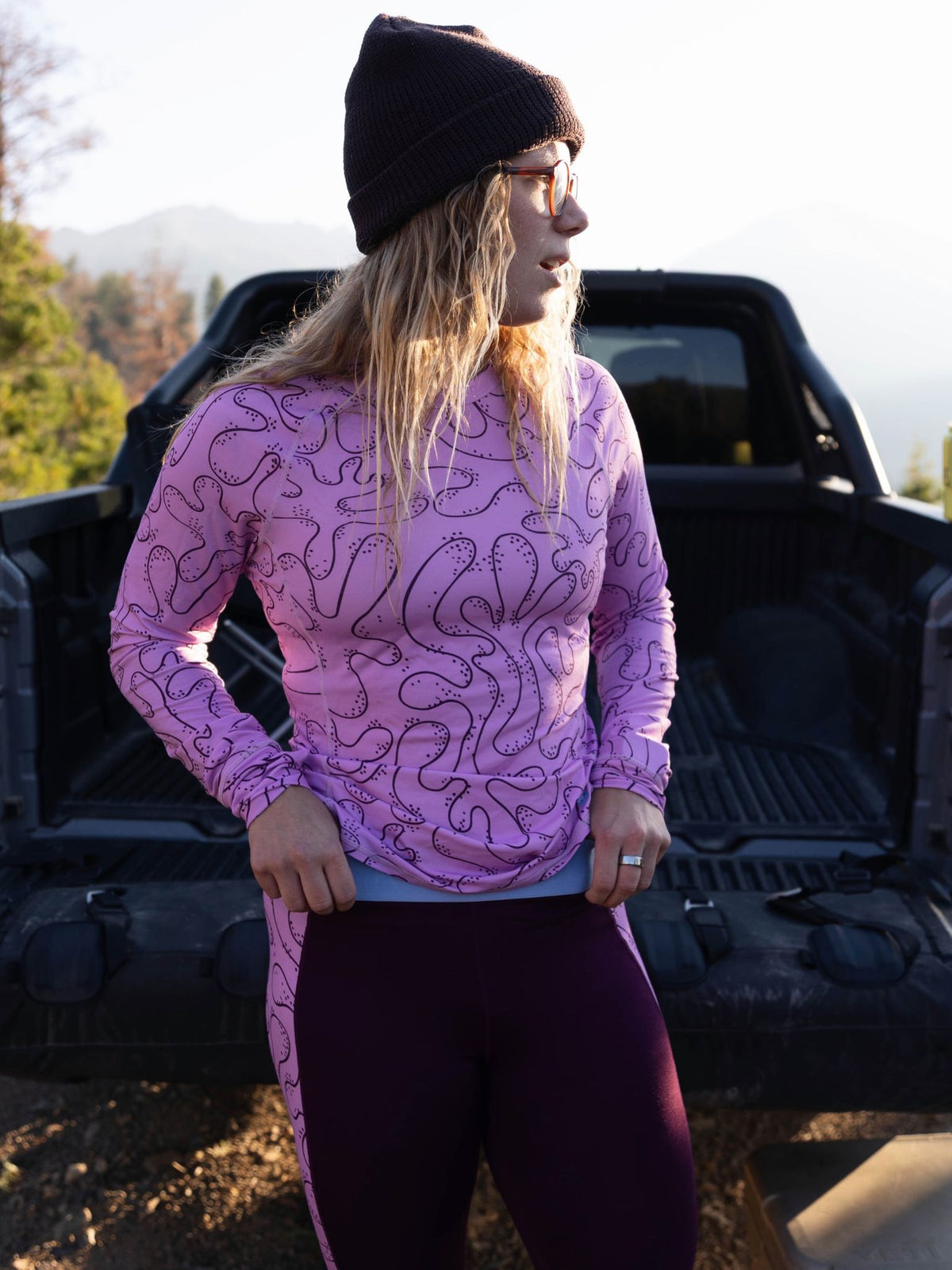 [Orchid Reef] Woman wearing an orchid reef Bassett LITE Raglan standing by a truck in the mountains at golden hour