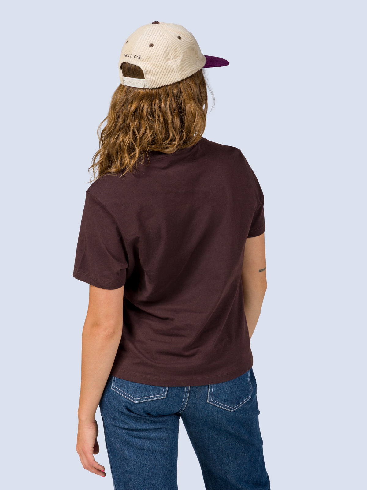 [Fondue] Back view of a model wearing the Fondue Graphic Tee in dark brown with a cream and purple Fondue trucker hat