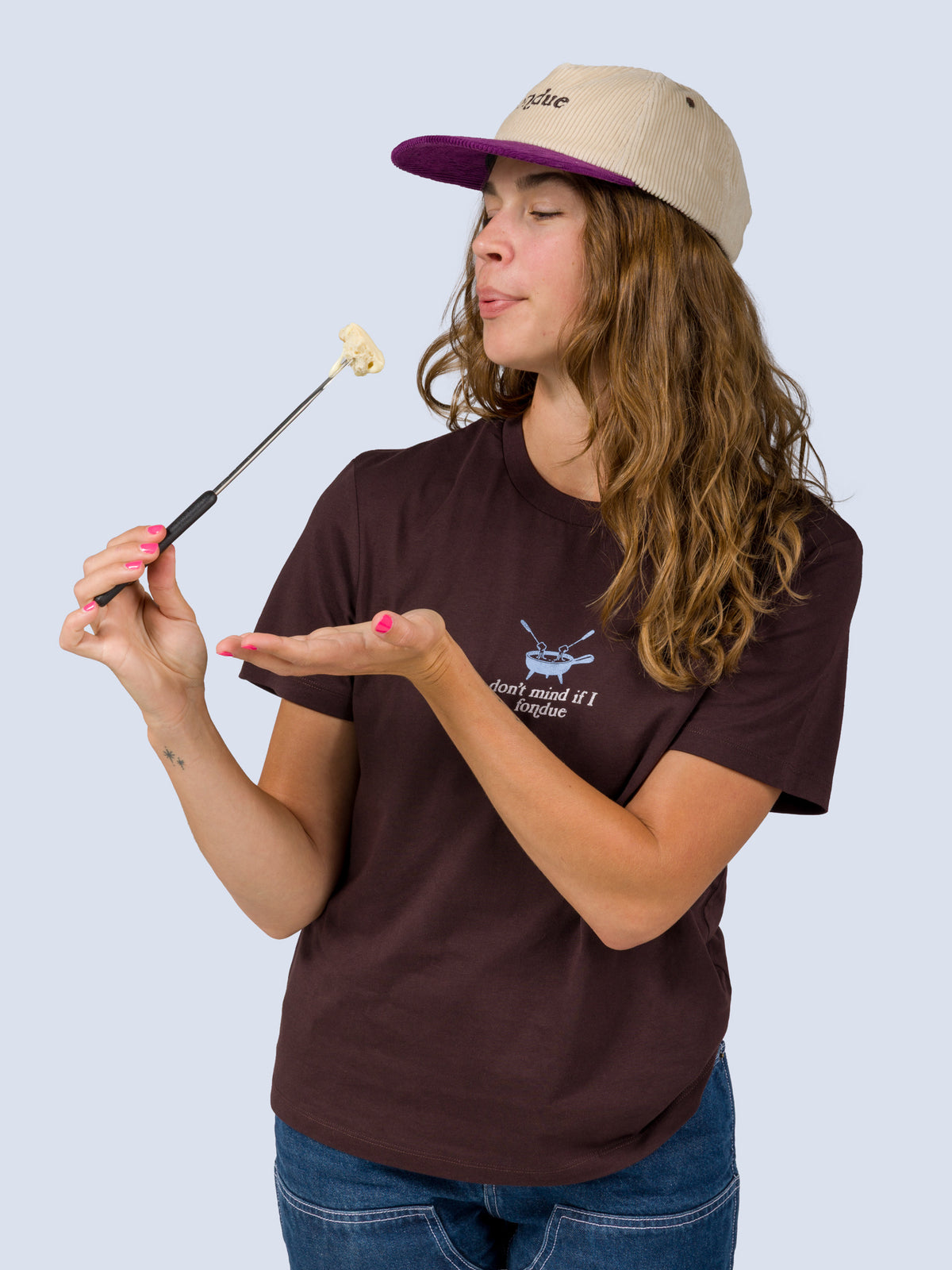 [Fondue] Model wearing the Fondue Graphic Tee in dark brown, holding a fondue fork with melted cheese near her mouth