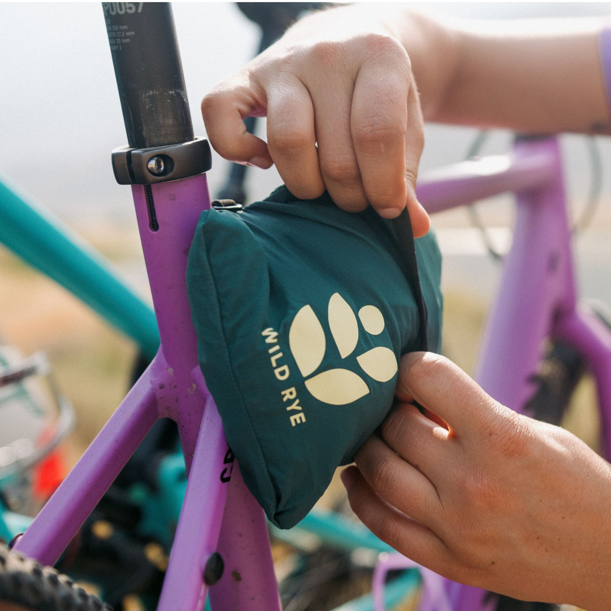 [Shaded Spruce] Person attaching the rustler windbreaker to their bike frame using the clip and stow functionality