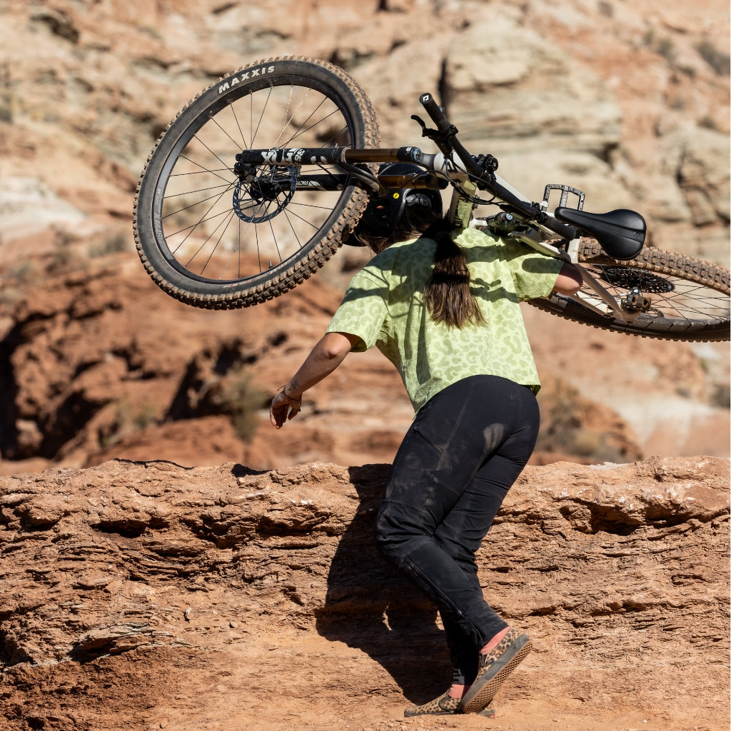 [Black] Woman hiking mountain bike up a rocky surface