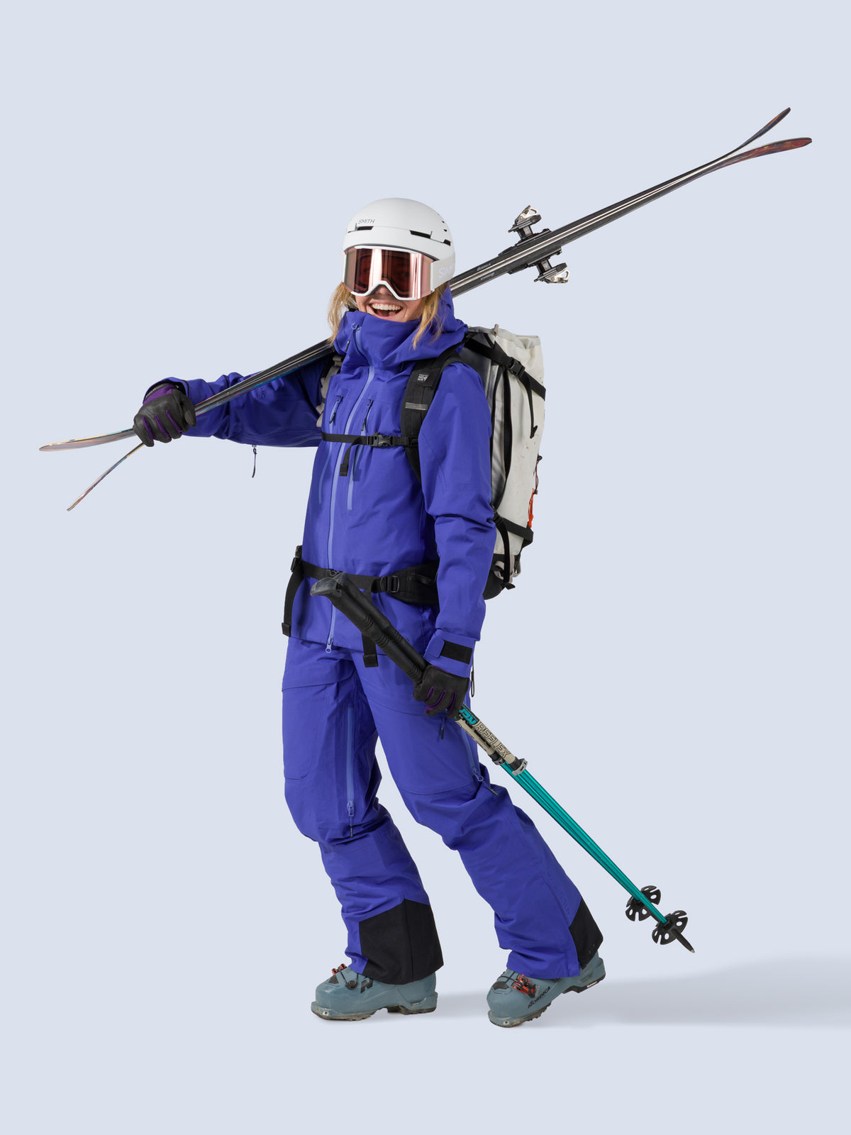 [Lapis] Heyburn 3L Bib in lapis blue, styled with the Heyburn 3L Jacket, on model carrying skis shot