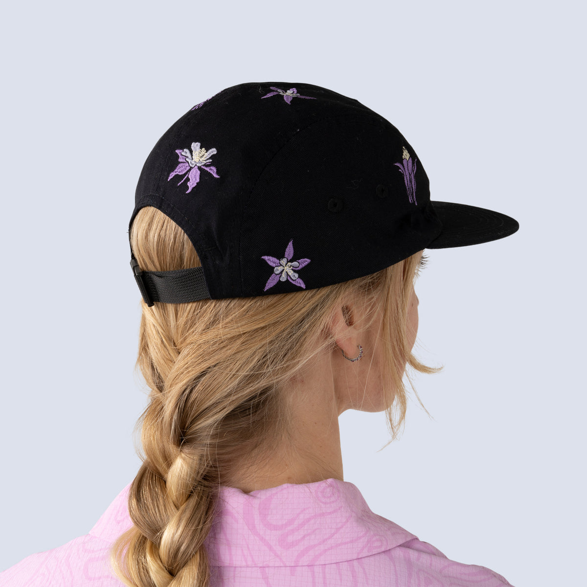 [Black Aquila Embroidery] Black baseball hat with floral embroidery worn by a person with blonde hair, against a light gray background